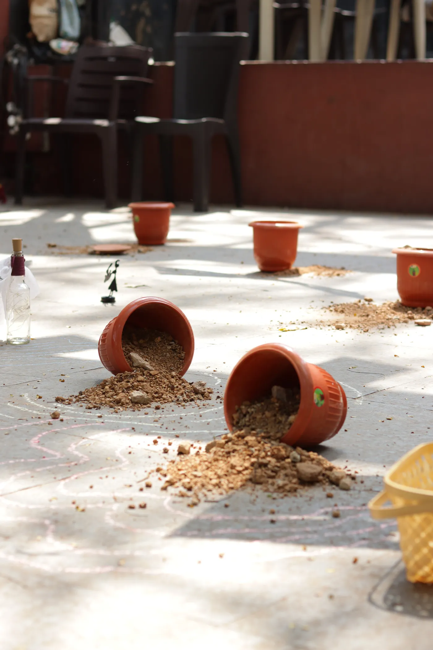 Terracotta pots tipped over on the ground, spilling earth across chalk lines.
