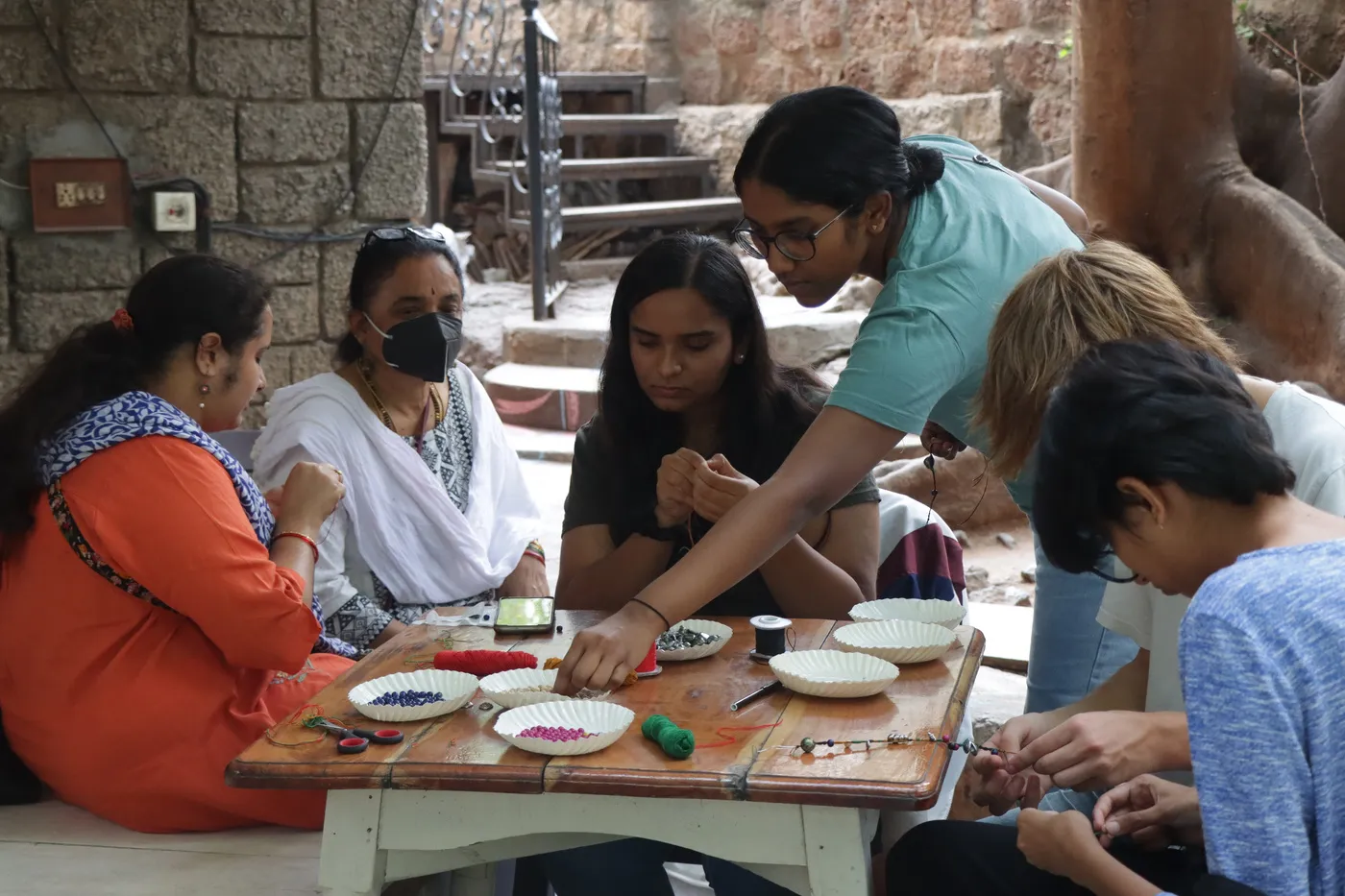 A group around a low table making friendship bracelets, plates of beads set out between them.
