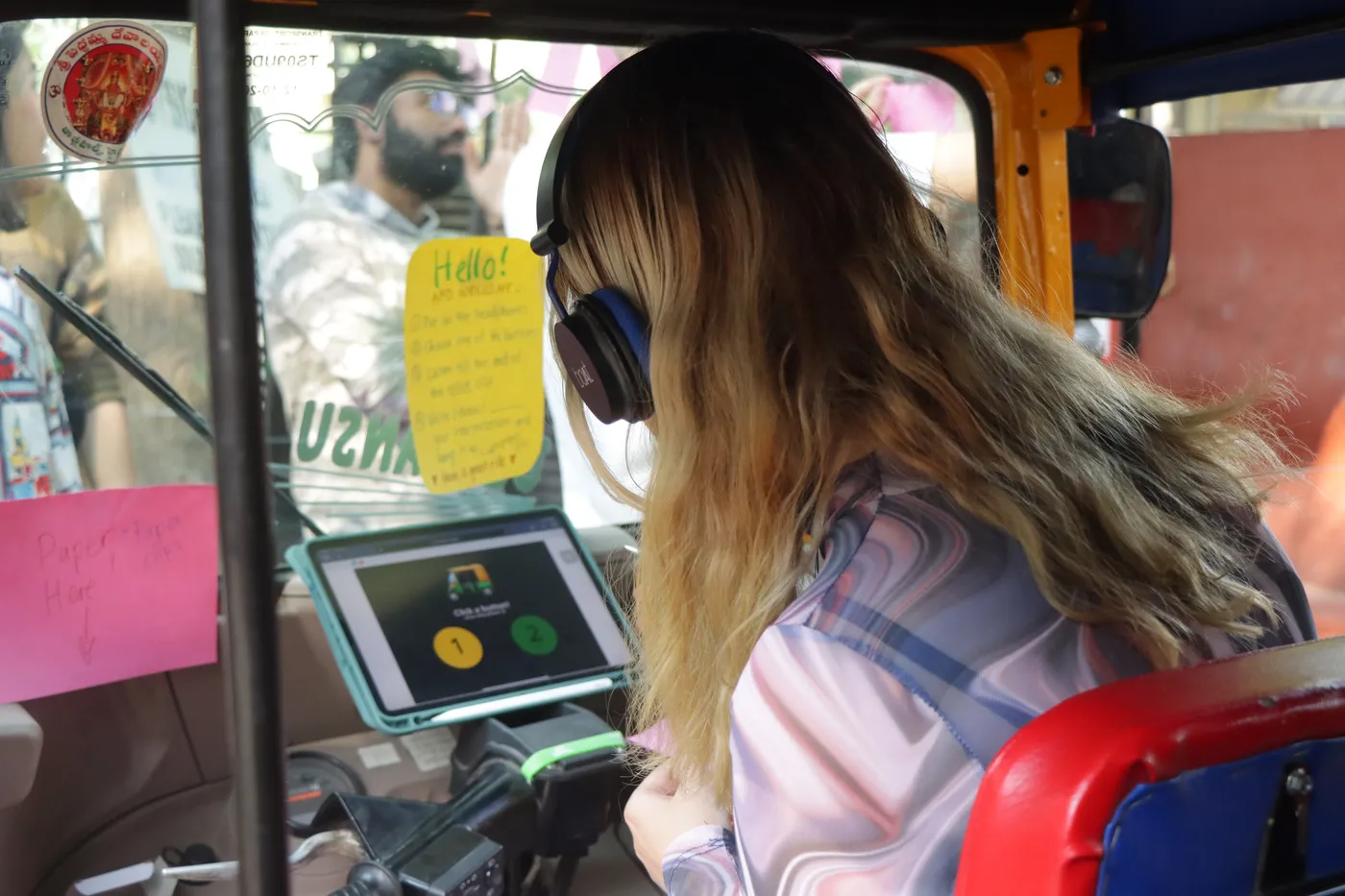 A visitor in headphones sitting in the auto's driver seat, a tablet propped in front of them and notes stuck to the frame.