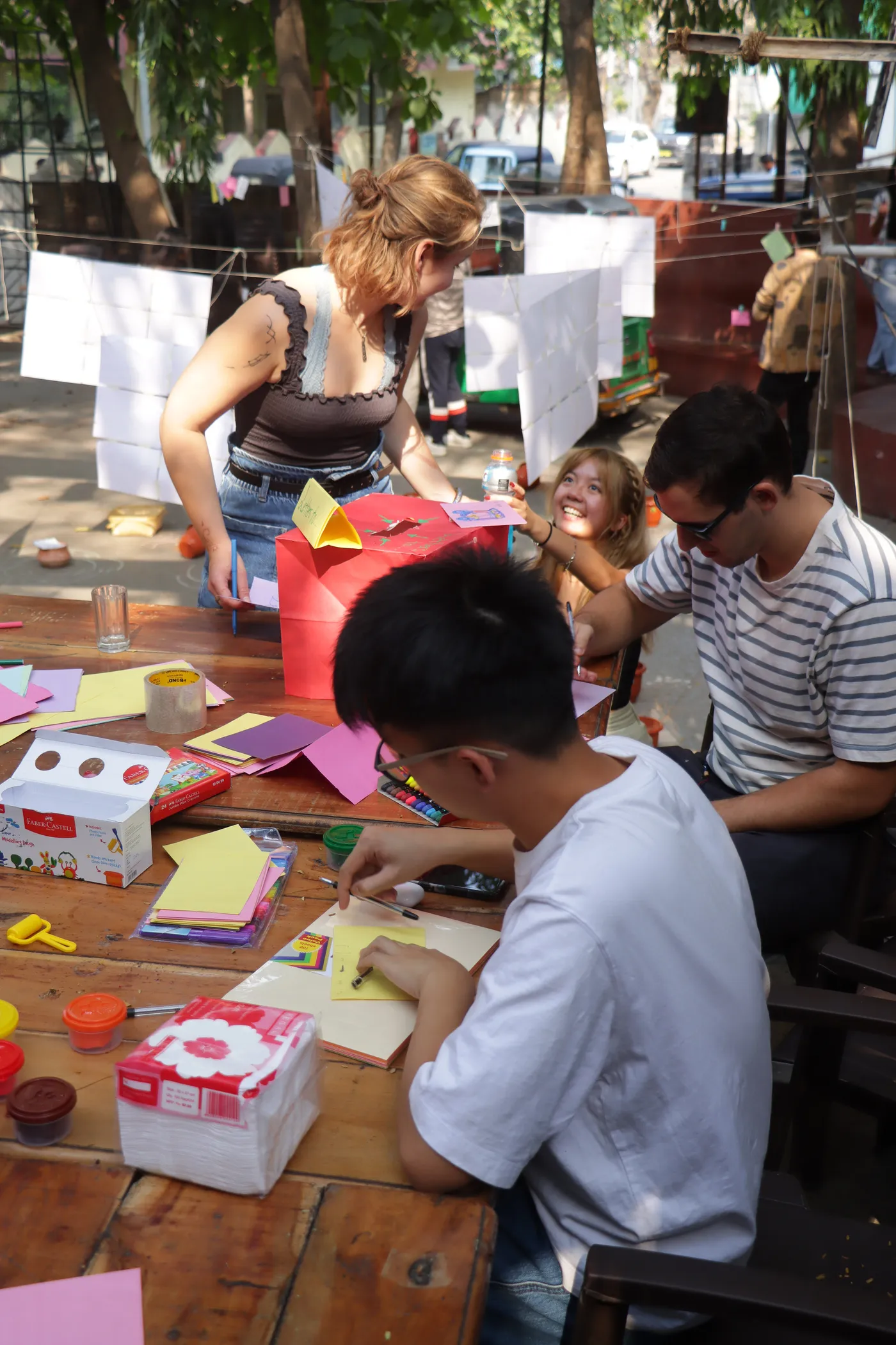 People gathered at a table covered in coloured paper, one of them folding a sheet.