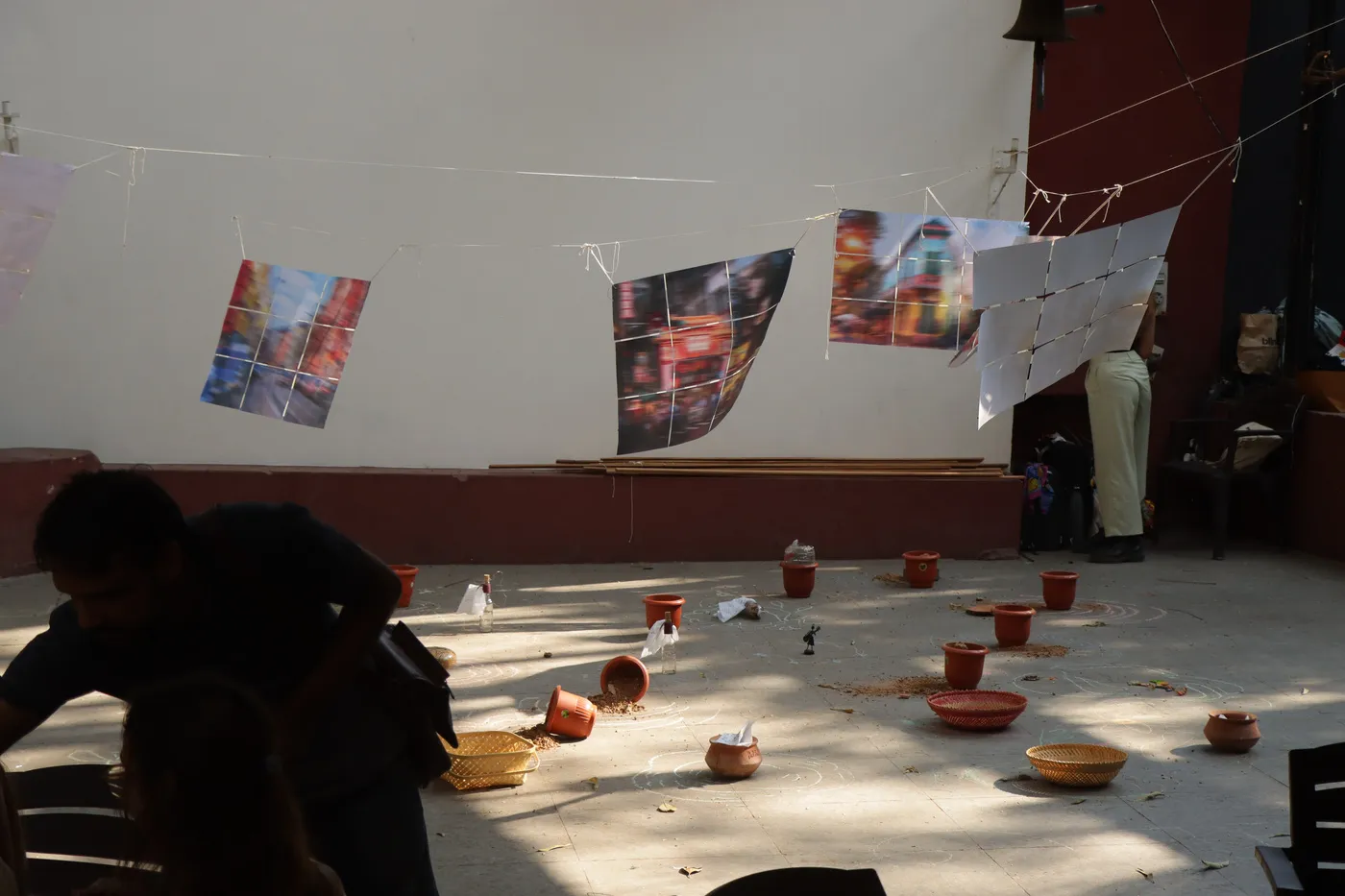 Blurred posters of city landmarks hung at angles across a white wall, with small clay pots and trinkets set out on the floor beneath them.