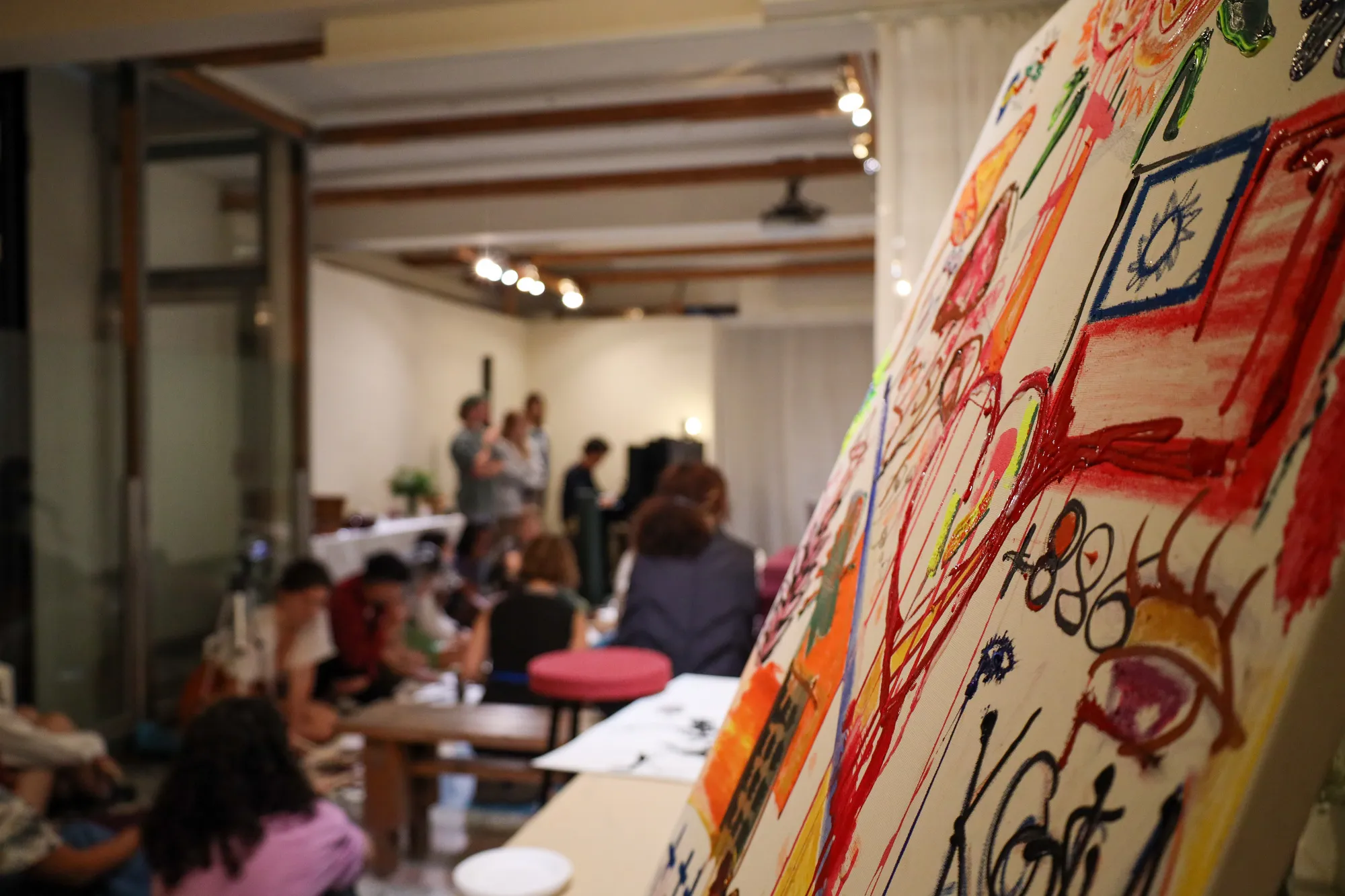 A dancer mid-movement on a large sheet of paper while a painter works at the edge of it and an audience watches from the floor.