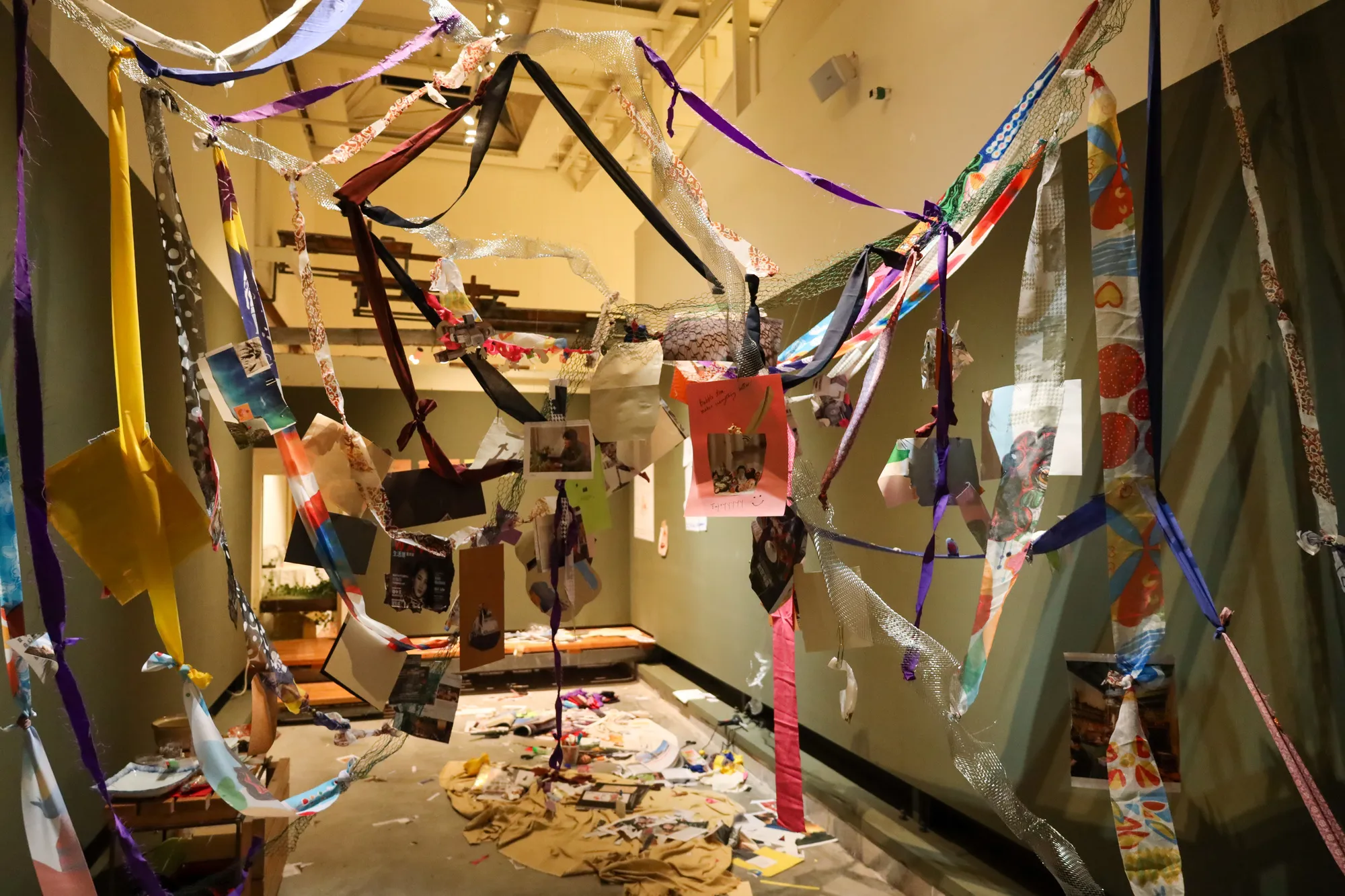 The hanging central web, a tangle of wire and collaged paper suspended above the room.